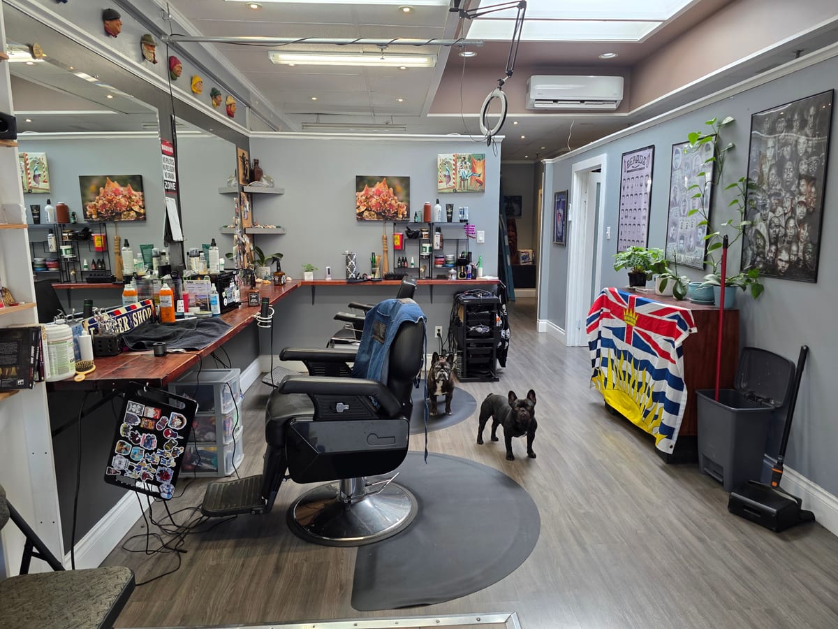 Inside The Edge: a barber chair on its mat, the long counter of products and mirrors, a French bulldog on the floor and the BC flag by the back wall